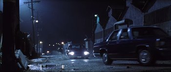 Movie still from “Dark Blue” (2002), directed by Ron Shelton – Cars driving down a street at night in the dark; Extreme Wide shot, Low angle