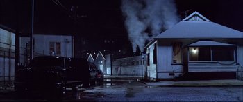 Movie still from “Dark Blue” (2002), directed by Ron Shelton – A car parked on the side of the road next to a building with smoke coming out of it; Extreme Wide shot, Low angle