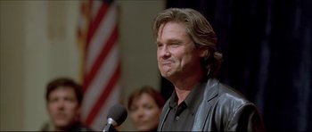 Movie still from “Dark Blue” (2002), directed by Ron Shelton – A man with long brown hair is speaking into a microphone; Close Up shot, Low angle
