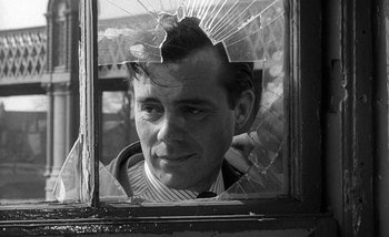 Movie still from “Darling” (1965), directed by John Schlesinger – A black and white photo of a man looking through a broken window; Close Up shot, Over the shoulder angle