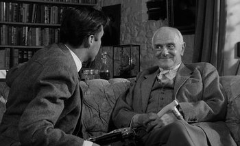 Movie still from “Darling” (1965), directed by John Schlesinger – A man sitting on a couch talking to another man; Medium shot, Over the shoulder angle