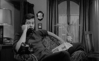 Movie still from “Darling” (1965), directed by John Schlesinger – A man sitting on top of a couch talking on the phone; Medium shot, High angle