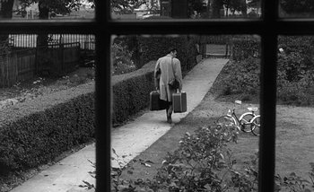 Movie still from “Darling” (1965), directed by John Schlesinger – A man walking down a sidewalk with two suitcases; Wide shot, High angle