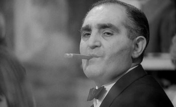 Movie still from “Darling” (1965), directed by John Schlesinger – An older man wearing a suit and bow tie smoking a cigarette; Close Up shot, Low angle