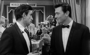 Movie still from “Darling” (1965), directed by John Schlesinger – A couple of men standing next to each other in a room; Medium shot, Over the shoulder angle