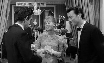 Movie still from “Darling” (1965), directed by John Schlesinger – Two men and a woman in formal wear at a formal event; Medium shot, Over the shoulder angle