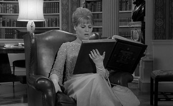 Movie still from “Darling” (1965), directed by John Schlesinger – A woman sitting in a chair looking at a book; Medium shot, Low angle
