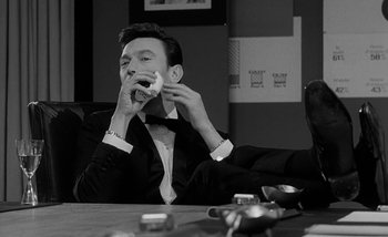 Movie still from “Darling” (1965), directed by John Schlesinger – A black and white photo of a man in a tuxedo eating a sandwich; Medium shot, Low angle