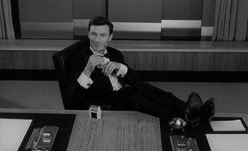 Movie still from “Darling” (1965), directed by John Schlesinger – A black and white photo of a man sitting on a couch; Medium shot, High angle