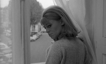 Movie still from “Darling” (1965), directed by John Schlesinger – A black - and - white photo of a woman standing in front of a window; Close Up shot, High angle