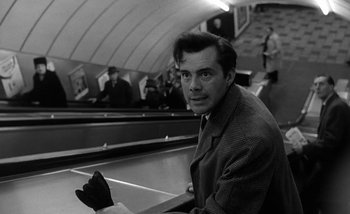 Movie still from “Darling” (1965), directed by John Schlesinger – A black and white photo of a man sitting on a train platform; Medium shot, Low angle