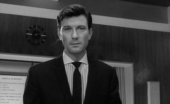 Movie still from “Darling” (1965), directed by John Schlesinger – Black and white photograph of a man wearing a suit and tie; Close Up shot, Low angle