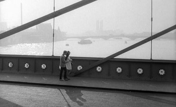 Movie still from “Darling” (1965), directed by John Schlesinger – Two people standing on the side of a bridge hugging; Wide shot, High angle