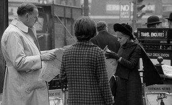 Movie still from “Darling” (1965), directed by John Schlesinger – A group of people standing on the street looking at newspapers; Medium shot, Over the shoulder angle