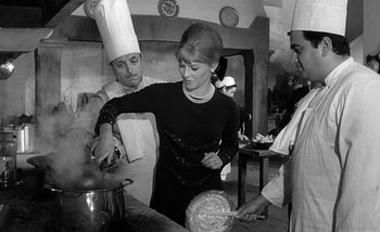 Movie still from “Darling” (1965), directed by John Schlesinger – A black and white photo of a woman cooking in a kitchen; Medium shot, High angle