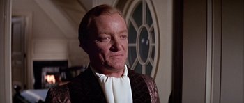 Movie still from “Darling Lili” (1970), directed by Blake Edwards – An older man wearing a suit and bow tie in front of a round window; Close Up shot, Over the shoulder angle