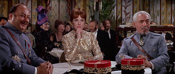 Movie still from “Darling Lili” (1970), directed by Blake Edwards – A woman sitting at a table in front of a group of people; Medium shot, Over the shoulder angle