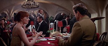 Movie still from “Darling Lili” (1970), directed by Blake Edwards – A group of people sitting around a table with plates and glasses; Medium shot, Over the shoulder angle
