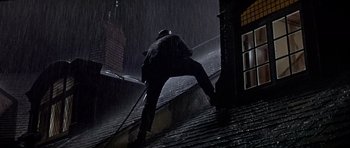Movie still from “Darling Lili” (1970), directed by Blake Edwards – A man standing on the side of a building in the pouring rain; Wide shot, Low angle