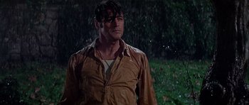 Movie still from “Darling Lili” (1970), directed by Blake Edwards – A man standing in the rain wearing a brown shirt; Medium shot, Low angle