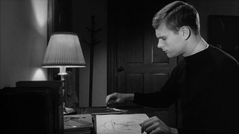 Movie still from “David and Lisa” (1962), directed by Frank Perry – A young man is drawing a picture in front of a lamp; Medium shot, High angle