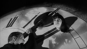 Movie still from “David and Lisa” (1962), directed by Frank Perry – A woman and a man looking up at a clock; Medium shot, Overhead angle