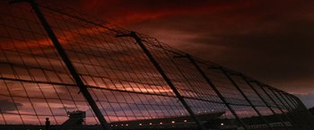 Movie still from “Days of Thunder” (1990), directed by Tony Scott – A wire fence is shown against a red sky; Extreme Wide shot, Low angle