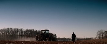 Movie still from “Days of Thunder” (1990), directed by Tony Scott – A man standing next to a tractor in a field; Extreme Wide shot, Low angle