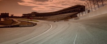 Movie still from “Days of Thunder” (1990), directed by Tony Scott – A car is driving down a race track at dusk; Extreme Wide shot, High angle
