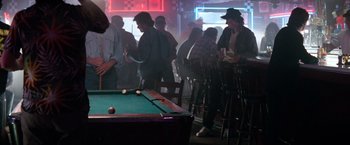Movie still from “Days of Thunder” (1990), directed by Tony Scott – A group of people standing around a pool table in a room; Wide shot, Over the shoulder angle