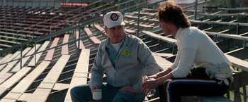 Movie still from “Days of Thunder” (1990), directed by Tony Scott – A man sitting on the bleachers with a cup of coffee; Medium shot, Over the shoulder angle