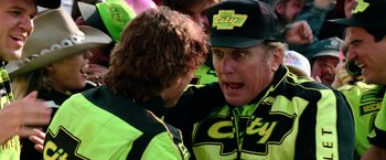 Movie still from “Days of Thunder” (1990), directed by Tony Scott – A man in yellow and black jacket talking to another man in a black hat; Close Up shot, Over the shoulder angle