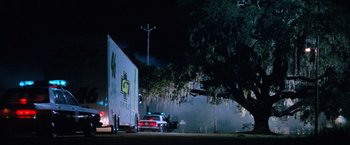 Movie still from “Days of Thunder” (1990), directed by Tony Scott – A police car is parked on the side of the road near a tree; Extreme Wide shot, Low angle