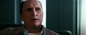 Movie still from “Days of Thunder” (1990), directed by Tony Scott – An older man looking into the distance with a serious look; Close Up shot, Over the shoulder angle