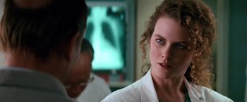 Movie still from “Days of Thunder” (1990), directed by Tony Scott – A woman in a white lab coat looking at the camera; Close Up shot, Over the shoulder angle