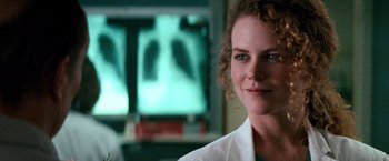 Movie still from “Days of Thunder” (1990), directed by Tony Scott – A woman in a white lab coat is smiling for the camera; Close Up shot, Over the shoulder angle