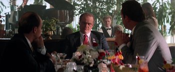 Movie still from “Days of Thunder” (1990), directed by Tony Scott – A man sitting at a table in front of other people; Medium shot, Over the shoulder angle