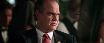 Movie still from “Days of Thunder” (1990), directed by Tony Scott – A man in a suit and red tie looking to his left; Close Up shot, Low angle