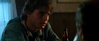 Movie still from “Days of Thunder” (1990), directed by Tony Scott – A man sitting at a table with a bottle of beer in front of him; Close Up shot, Over the shoulder angle