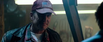 Movie still from “Days of Thunder” (1990), directed by Tony Scott – An older man wearing a baseball cap and a plaid shirt; Close Up shot, Low angle