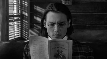 Movie still from “Dead Man” (1995), directed by Jim Jarmusch – A man with long hair and glasses reading a newspaper; Close Up shot, Over the shoulder angle