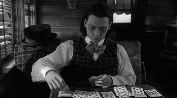 Movie still from “Dead Man” (1995), directed by Jim Jarmusch – A man sitting at a table with playing cards in front of him; Medium shot, Over the shoulder angle