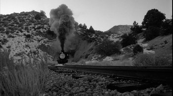 Movie still from “Dead Man” (1995), directed by Jim Jarmusch – A train traveling down train tracks next to a forest; Extreme Wide shot, Low angle