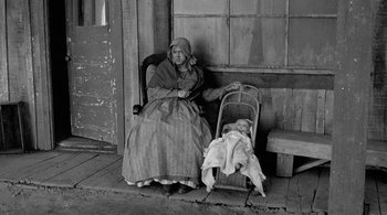 Movie still from “Dead Man” (1995), directed by Jim Jarmusch – An old woman sitting in a chair next to a baby in a stroller; Wide shot, High angle