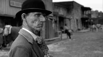 Movie still from “Dead Man” (1995), directed by Jim Jarmusch – A man wearing a hat and a tie standing in front of a building; Close Up shot, Low angle