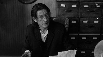 Movie still from “Dead Man” (1995), directed by Jim Jarmusch – A man sitting at a desk in front of papers; Close Up shot, Over the shoulder angle