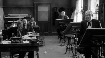 Movie still from “Dead Man” (1995), directed by Jim Jarmusch – A group of people sitting at a table with musical instruments; Wide shot, High angle
