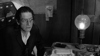 Movie still from “Dead Man” (1995), directed by Jim Jarmusch – A man sitting in front of a table with papers on it; Close Up shot, Over the shoulder angle