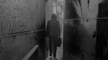 Movie still from “Dead Man” (1995), directed by Jim Jarmusch – A man walking down a hallway holding a suitcase; Wide shot, High angle