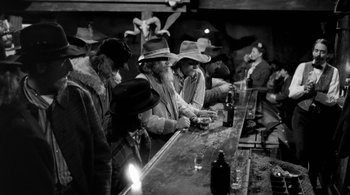 Movie still from “Dead Man” (1995), directed by Jim Jarmusch – A black and white photo of a group of men sitting at a bar; Wide shot, High angle